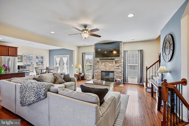 living room featuring hardwood / wood-style flooring, a ceiling fan, stairs, and a stone fireplace