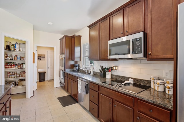 kitchen with appliances with stainless steel finishes, dark stone counters, a sink, and light tile patterned floors