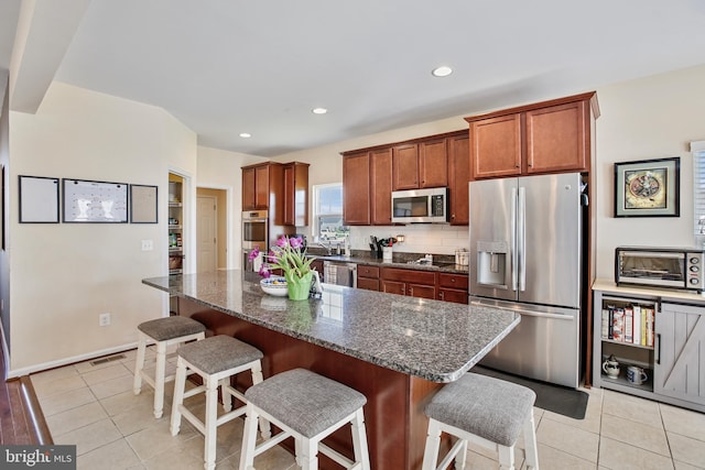 kitchen with a toaster, stainless steel appliances, light tile patterned flooring, a kitchen island, and a kitchen bar