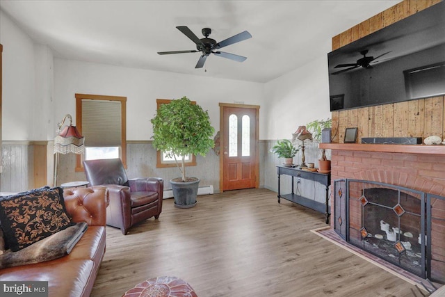 living room featuring baseboard heating, wood finished floors, ceiling fan, and a wainscoted wall