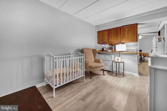 bedroom with light wood-type flooring, freestanding refrigerator, baseboards, and a nursery area