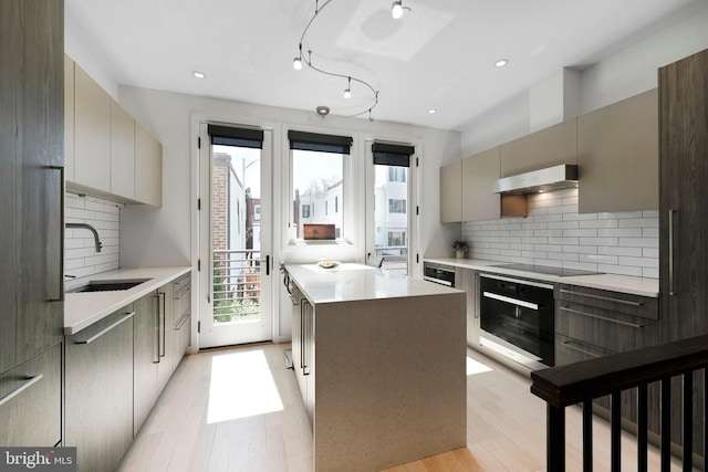 kitchen with a sink, modern cabinets, under cabinet range hood, and black appliances