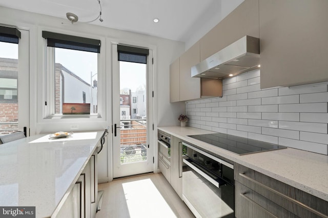 kitchen featuring decorative backsplash, extractor fan, light wood-type flooring, light stone counters, and black appliances
