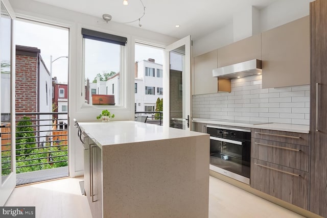 kitchen featuring decorative backsplash, black oven, modern cabinets, and a kitchen island