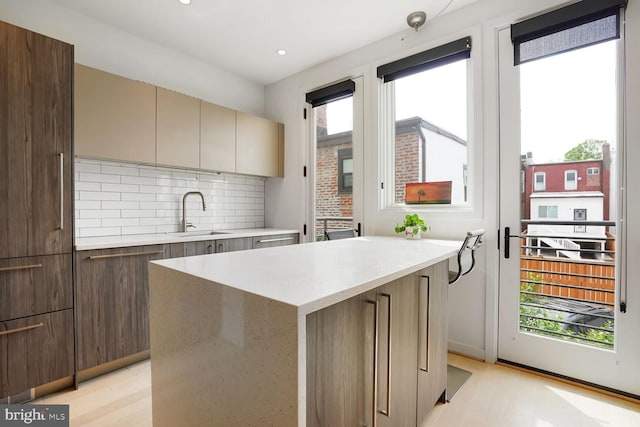 kitchen featuring a sink, modern cabinets, light wood finished floors, and tasteful backsplash