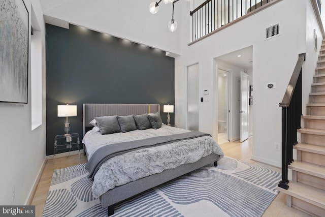 bedroom featuring baseboards, visible vents, a high ceiling, and light wood finished floors