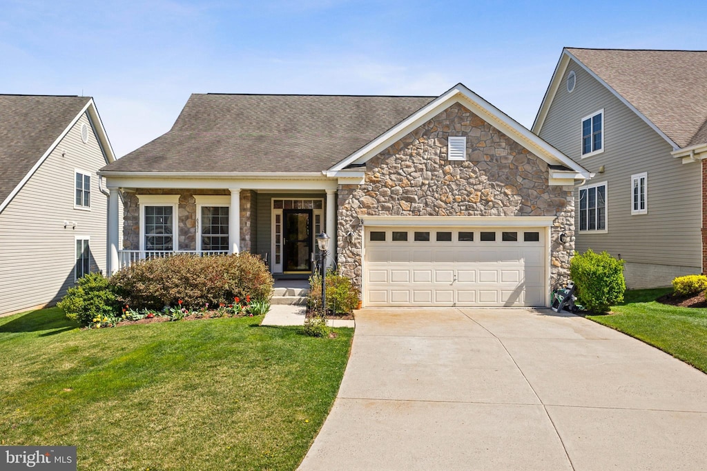 view of front of property featuring a front lawn, stone siding, a garage, and driveway