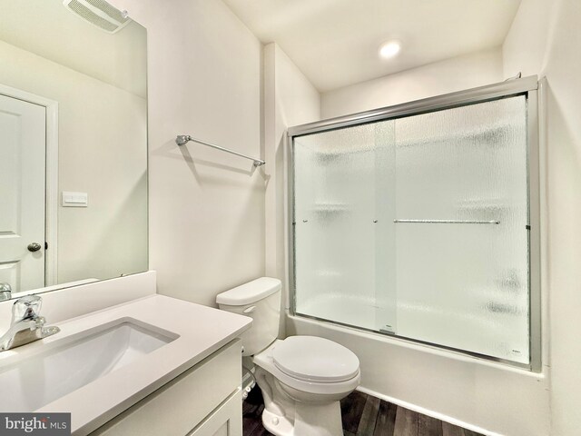 bathroom featuring vanity, visible vents, toilet, wood finished floors, and bath / shower combo with glass door