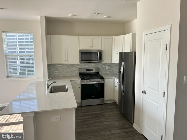 kitchen featuring tasteful backsplash, a peninsula, dark wood-type flooring, appliances with stainless steel finishes, and a sink