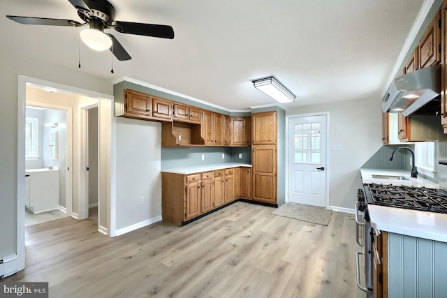 kitchen with brown cabinetry, under cabinet range hood, stainless steel range with gas cooktop, and a sink