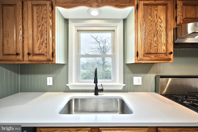 kitchen featuring a sink, wall chimney range hood, light countertops, and brown cabinets