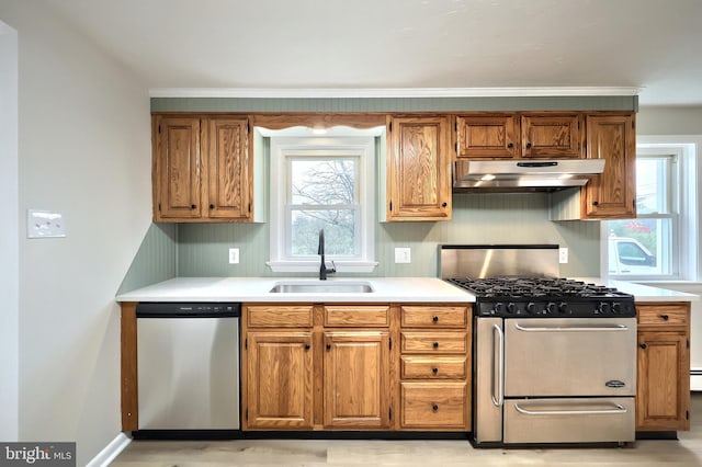 kitchen with light countertops, under cabinet range hood, brown cabinetry, appliances with stainless steel finishes, and a sink