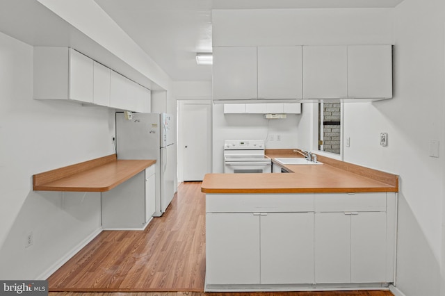 kitchen with white cabinets, baseboards, a sink, white appliances, and a peninsula