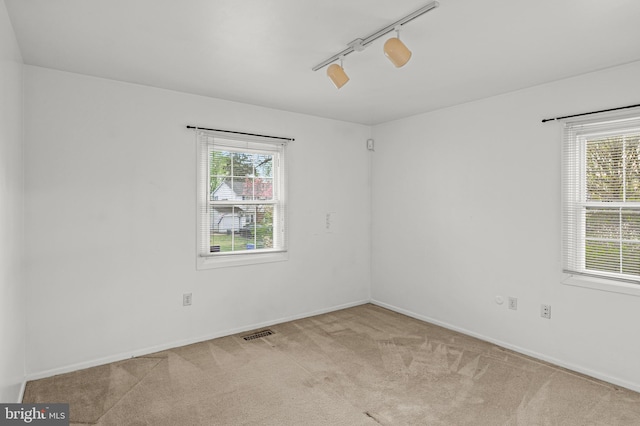 carpeted empty room featuring visible vents, baseboards, and rail lighting