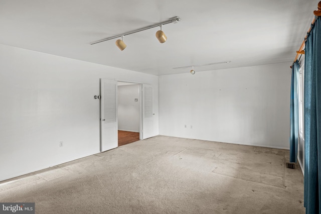 carpeted empty room featuring rail lighting and visible vents