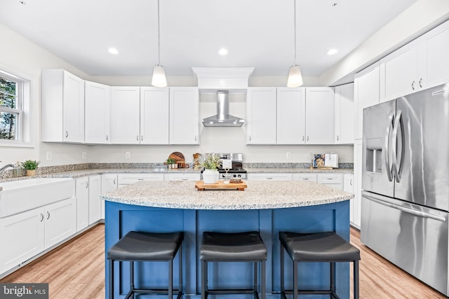 kitchen with a sink, wall chimney range hood, light wood-style floors, stainless steel appliances, and a breakfast bar area