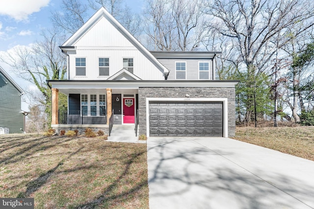 view of front of property with a front yard, an attached garage, stone siding, covered porch, and driveway