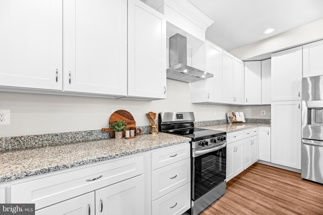 kitchen featuring stainless steel appliances, light wood-type flooring, wall chimney exhaust hood, and white cabinetry