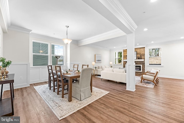 dining space featuring a fireplace, crown molding, recessed lighting, wood finished floors, and a wainscoted wall