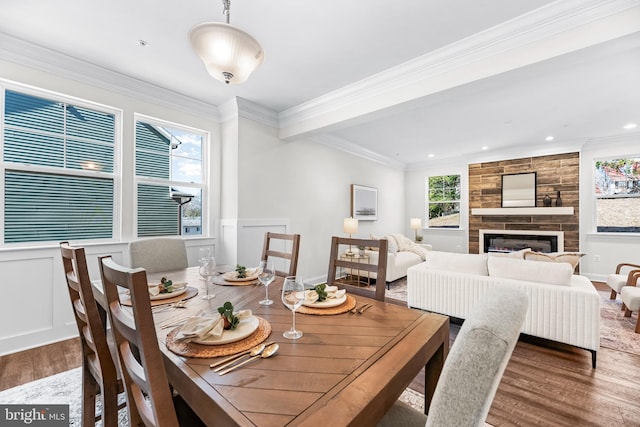 dining space with ornamental molding, wainscoting, a decorative wall, a tile fireplace, and wood finished floors