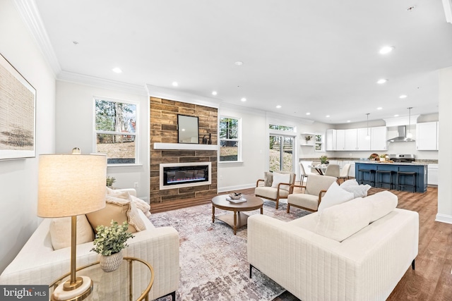 living room featuring a large fireplace, ornamental molding, light wood finished floors, and recessed lighting