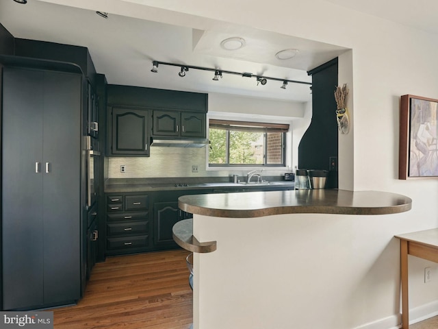 kitchen with dark countertops, dark wood finished floors, a peninsula, decorative backsplash, and under cabinet range hood