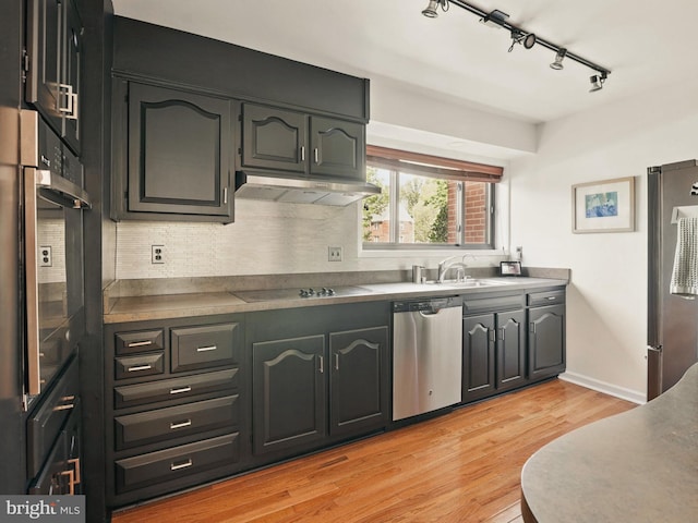 kitchen with a sink, light wood-style floors, under cabinet range hood, rail lighting, and appliances with stainless steel finishes