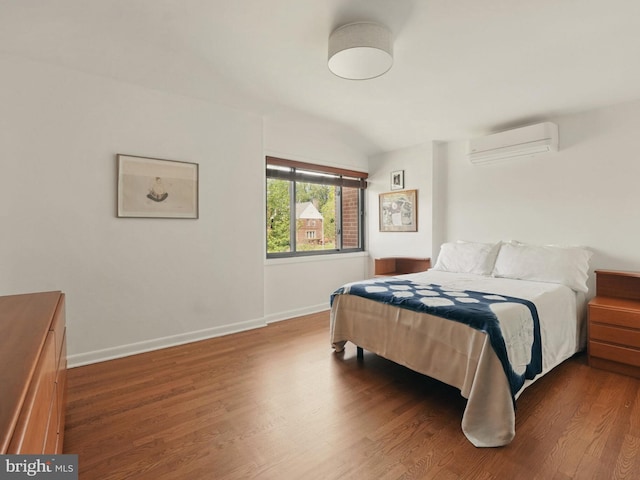 bedroom with an AC wall unit, baseboards, and wood finished floors