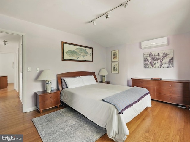 bedroom featuring a wall mounted AC, rail lighting, wood finished floors, baseboards, and lofted ceiling