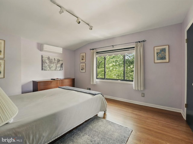 bedroom with track lighting, wood finished floors, lofted ceiling, baseboards, and a wall mounted AC