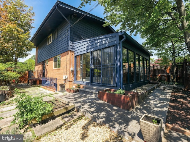 back of property featuring fence, a sunroom, and brick siding