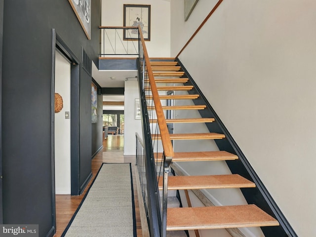 stairway with wood finished floors, a high ceiling, and visible vents