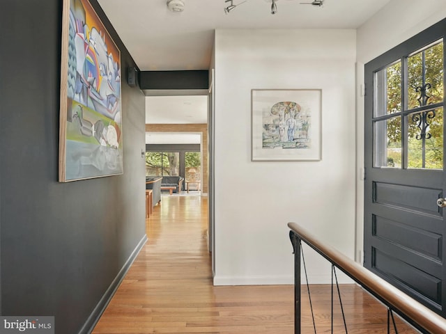 hallway with light wood-style floors, baseboards, and an upstairs landing