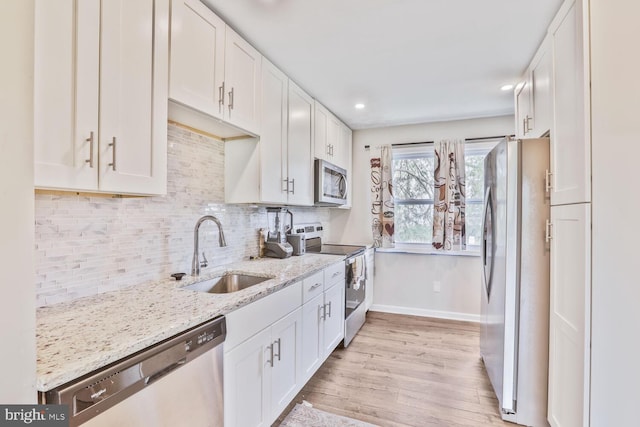 kitchen with stainless steel appliances, backsplash, a sink, baseboards, and light wood-style flooring