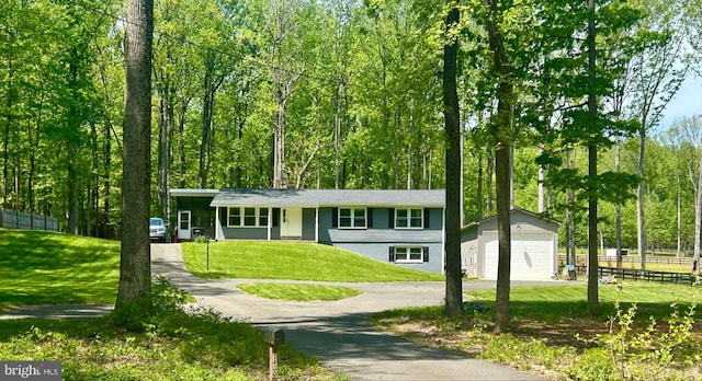 view of front facade with fence, a front lawn, a detached garage, an outbuilding, and driveway