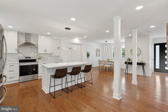 kitchen with wall chimney range hood, stainless steel electric range, a breakfast bar, white cabinets, and a kitchen island