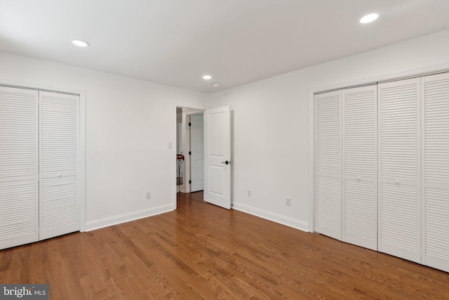 unfurnished bedroom with multiple closets, wood finished floors, and recessed lighting