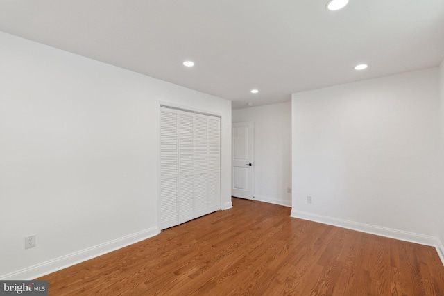 unfurnished bedroom with recessed lighting, wood finished floors, a closet, and baseboards