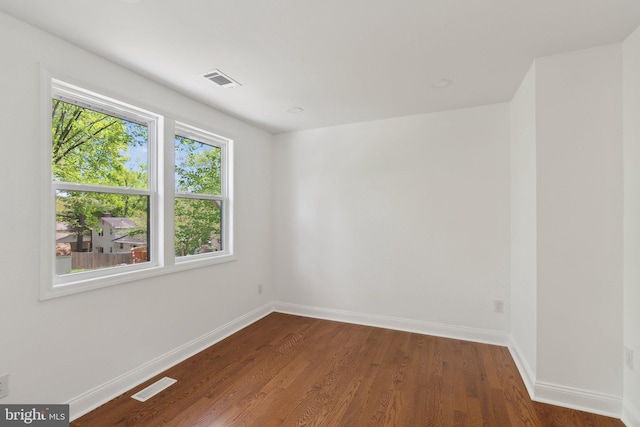 unfurnished room with baseboards, dark wood-style flooring, and visible vents