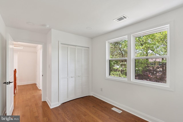 unfurnished bedroom with visible vents, wood finished floors, baseboards, and a closet