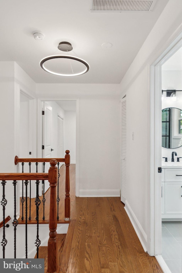 hallway with wood finished floors, visible vents, baseboards, and an upstairs landing