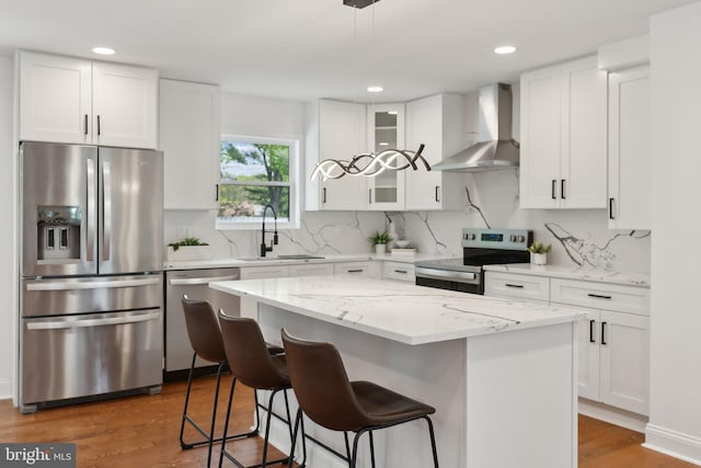 kitchen with stainless steel appliances, wood finished floors, a sink, wall chimney exhaust hood, and a breakfast bar area