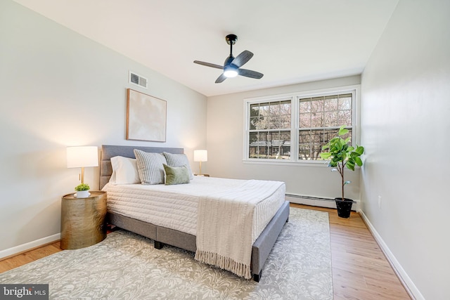 bedroom with baseboards, light wood-style floors, a baseboard radiator, and visible vents