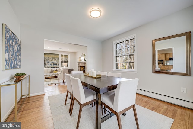 dining area featuring a brick fireplace, a baseboard heating unit, light wood-style floors, and baseboards
