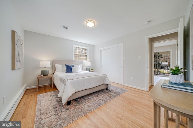 bedroom with a baseboard radiator, multiple windows, visible vents, and light wood-style floors