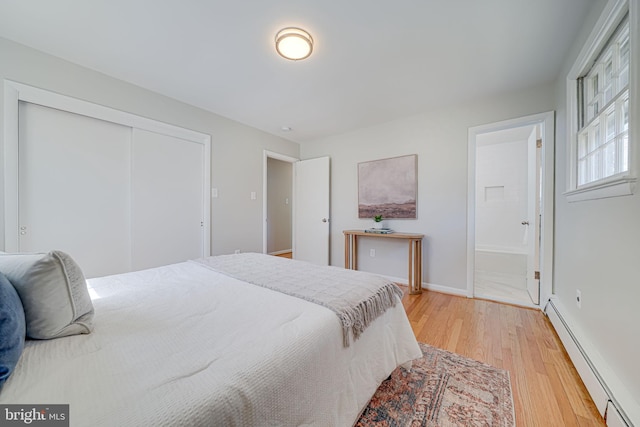 bedroom with a closet, baseboards, light wood-style floors, baseboard heating, and connected bathroom