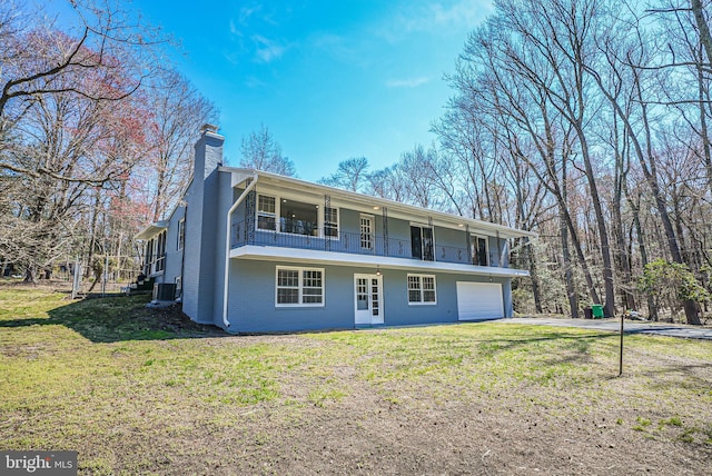 back of property with a yard, a chimney, driveway, and a balcony