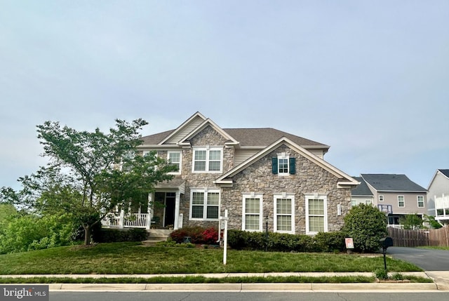 view of front facade with a front lawn, fence, and stone siding