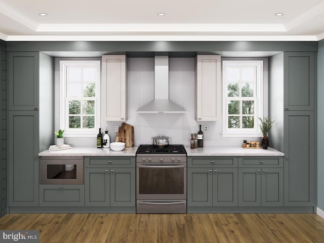 kitchen featuring wall chimney range hood, gas range, light countertops, a raised ceiling, and built in microwave