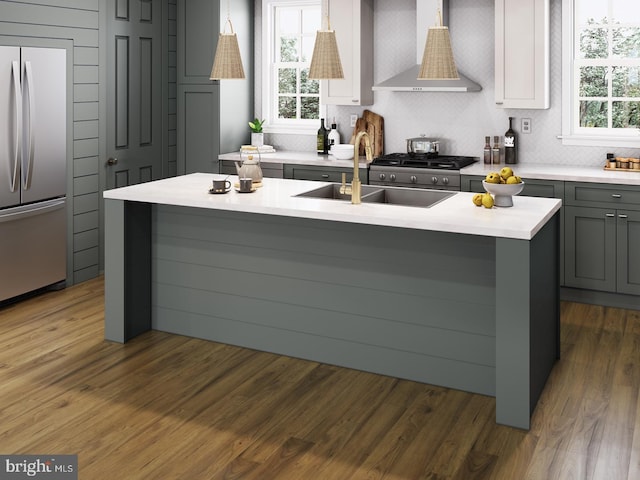 kitchen with stainless steel refrigerator, wall chimney range hood, gray cabinets, a sink, and light countertops